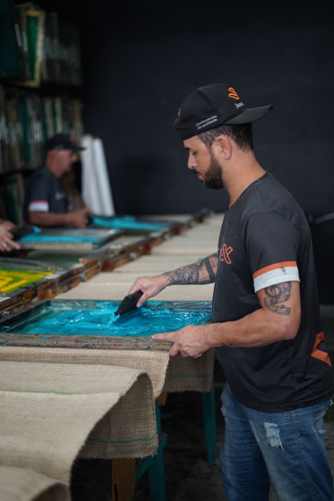 Operador JX aplicando tinta na tela de serigrafia sobre saca de juta