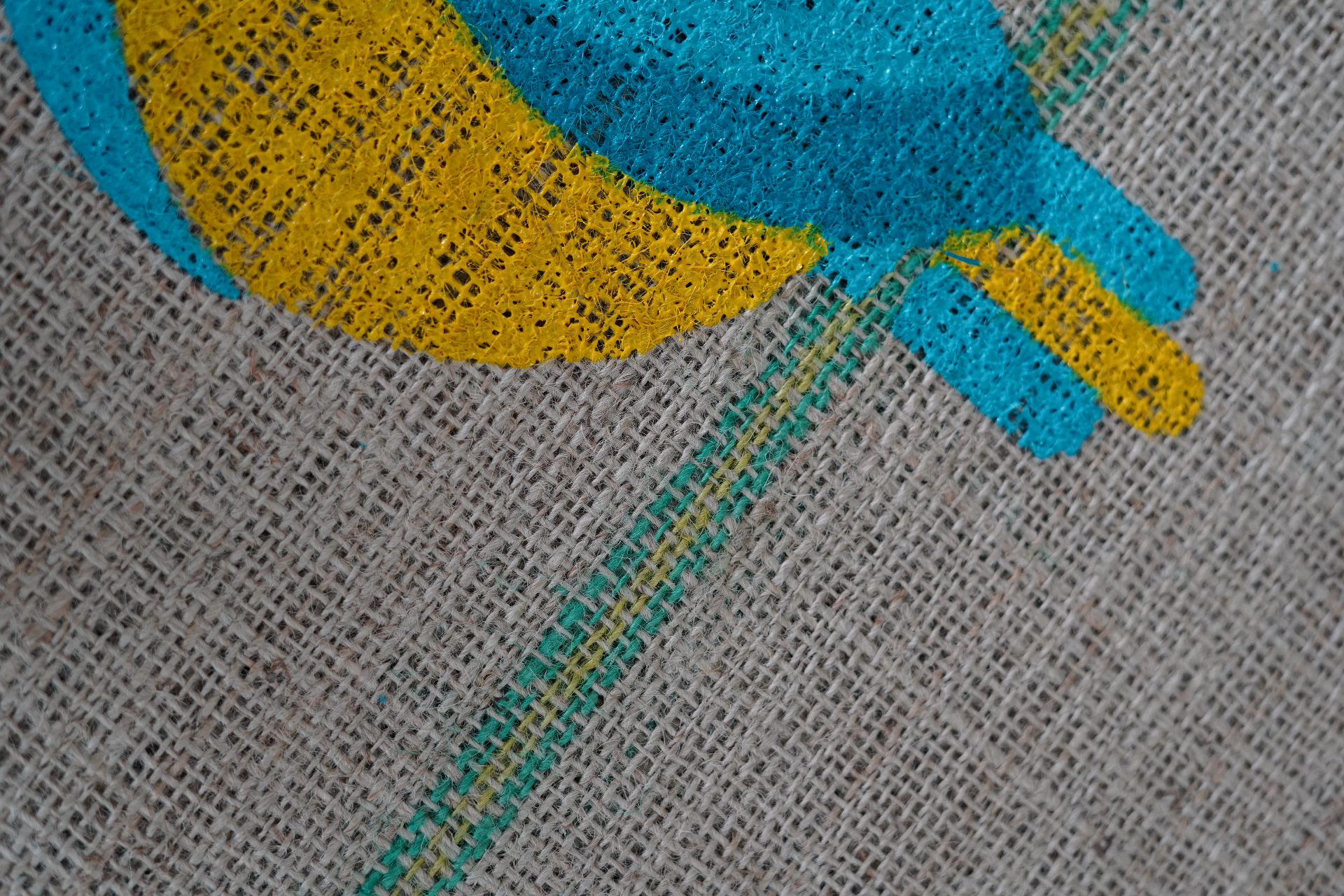 Detalhe macro de marcação JX em saca de juta — cores vivas em amarelo e azul